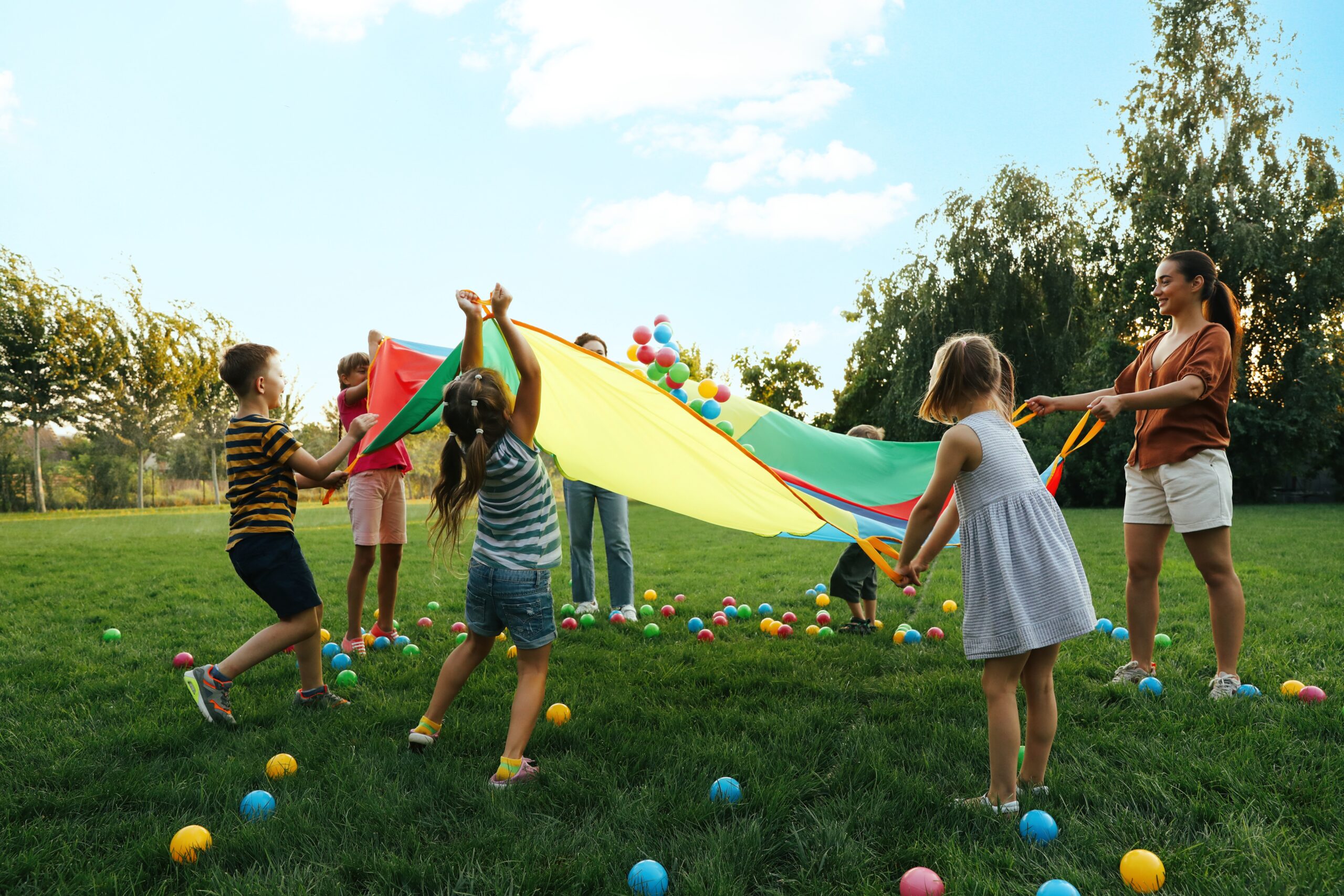 Group,Of,Children,And,Teacher,Playing,With,Rainbow,Playground,Parachute